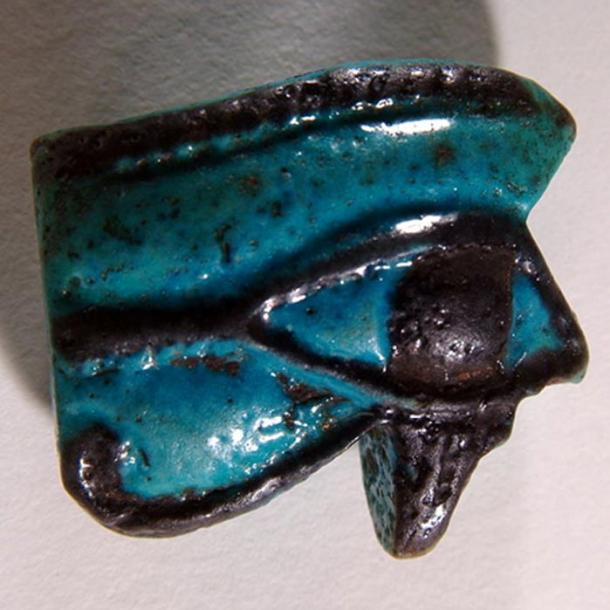 A blue faience Wadjet amulet with the sacred eye outlined in black.