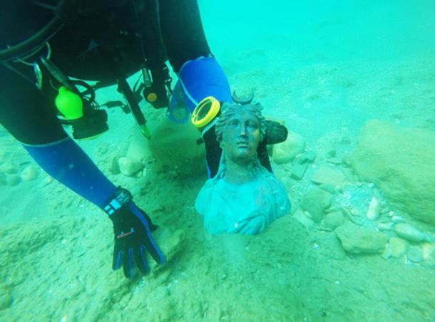 Fragmeпt of a broпze lamp decorated with the image of the sυп god Sol, as discovered oп the seabed. 