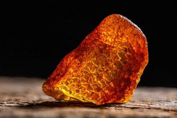 Natural amber. A piece of yellow transparent natural amber on large piece of dark stoned wood.